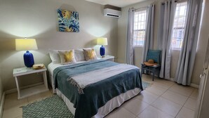 A neatly arranged bedroom with a bed, two bedside tables with lamps, a wall-mounted air conditioner, and a window with curtains.