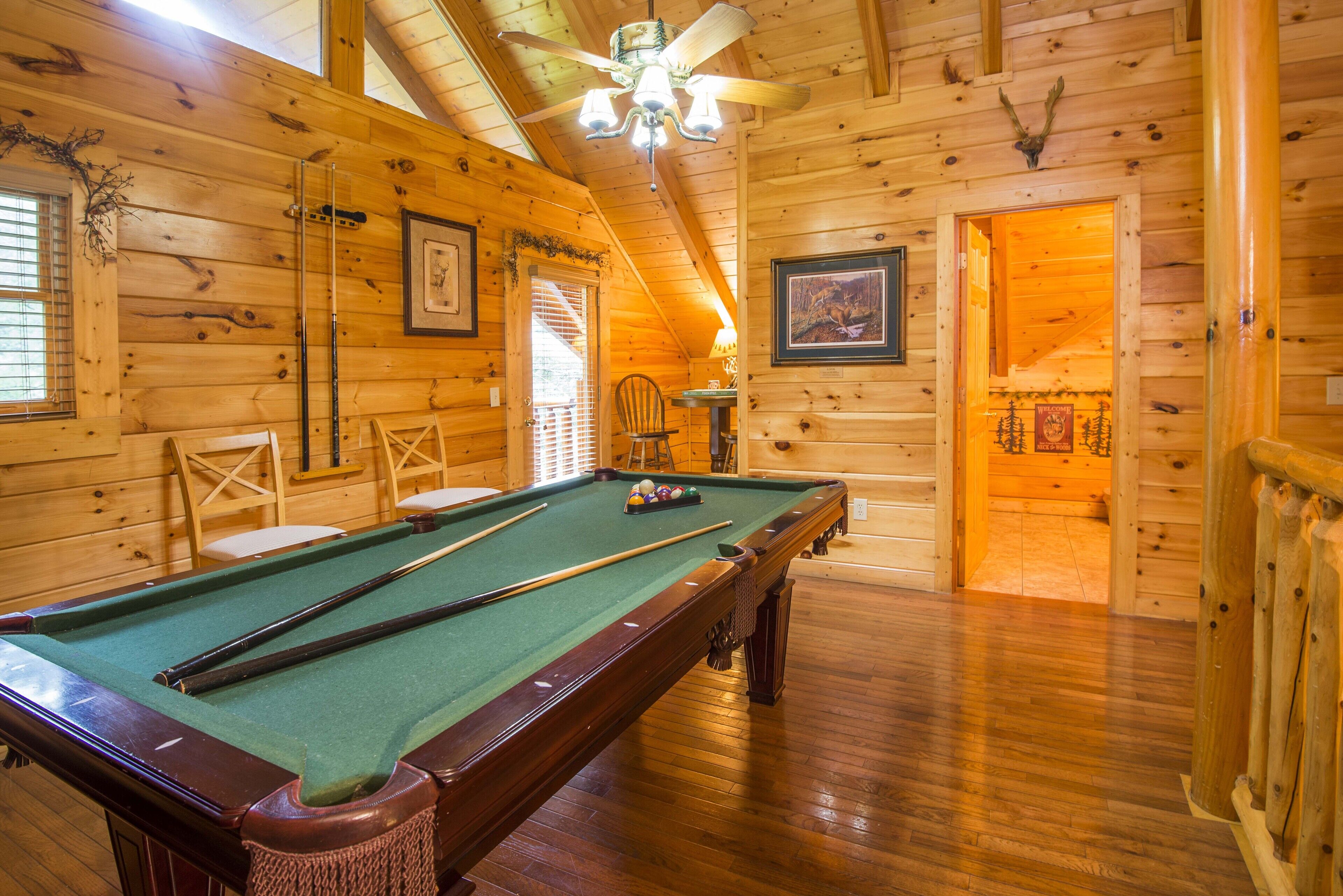 Une cabane en bois avec une table de billard, un ventilateur de plafond et un tableau encadré au mur.