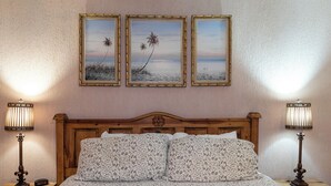 A bedroom with a wooden headboard, a floral-patterned bedspread, two bedside lamps, and three framed beach paintings on the wall.