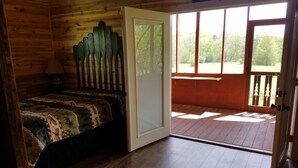 A wooden cabin bedroom with a bed, a window, and a door leading to an outdoor deck. - SUNDANCER CABIN CADDO RIVER!!!!!   GREAT GETAWAY !!!!!!!! River Access!! (Glenwood)