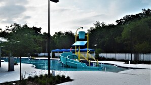 A water park with a blue slide, a pool, and a fenced area. - Spacious Modern Retreat for Family Fun Near Tampa! (Riverview)