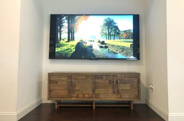 A flat-screen TV mounted on a wall above a wooden cabinet. - Spacious Modern Retreat for Family Fun Near Tampa! (Riverview)