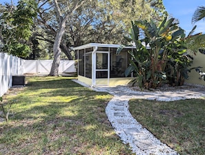 Relax in a serene backyard oasis with a sheltered patio area surrounded by lush greenery and a white picket fence.