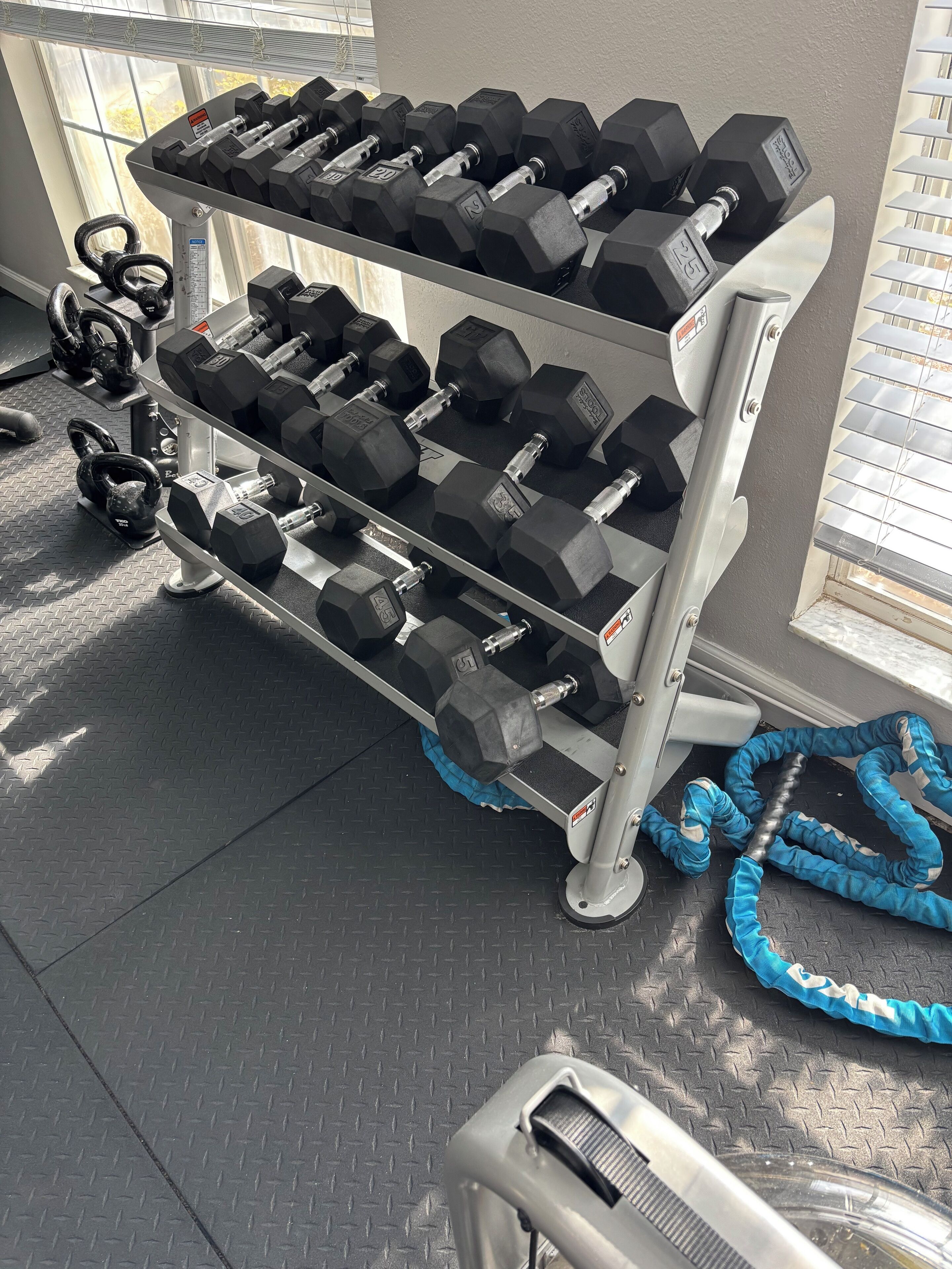 Une salle de sport équipée d’un porte-haltères, de kettlebells et d’un élastique de résistance bleu.