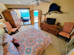A spacious bedroom with a large bed, a television, and a view of the ocean through a sliding door.