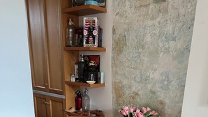 En brun läderfåtölj med en mönstrad kudde, ett litet sidobord med en vas med rosa blommor och en rustik vägg.