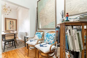 A room with a dining area, two chairs with nautical-themed cushions, a bookshelf with books, and a large map on the wall.