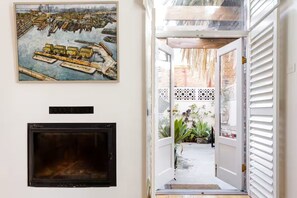 A hallway with a fireplace, a painting of a cityscape, and a view of a garden through an open door.
