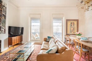 A living room with a sofa, a TV, a dining table with chairs, and a window with a view.