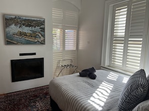 Una camera da letto con un letto, un quadro, un camino e una finestra con persiane.