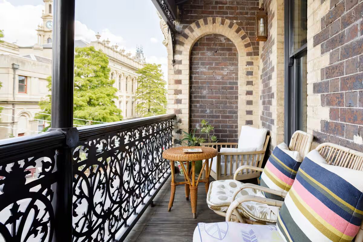 A balcony with wicker furniture, a small table, and a view of a historic building.