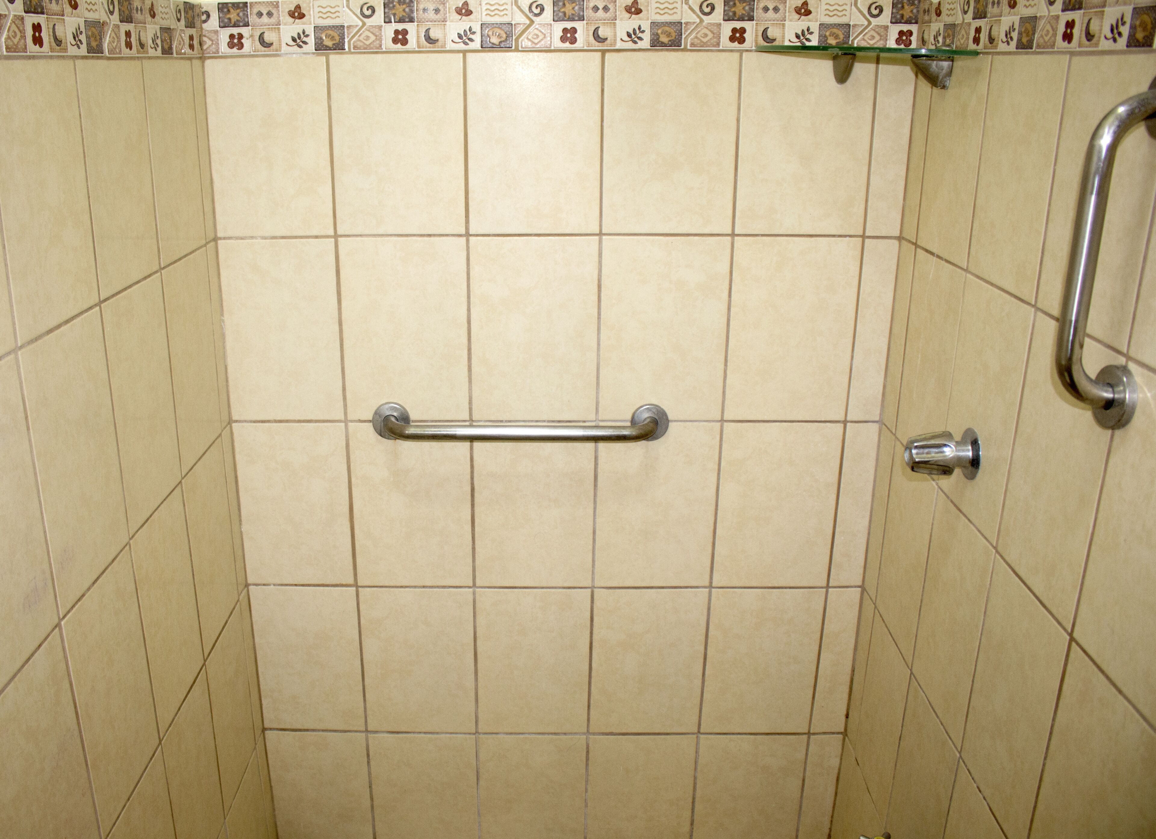 A bathroom with beige tiles, a grab bar, and a shower head.