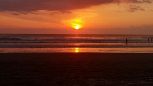 Un atardecer sobre el océano con olas y algunas personas en la playa.