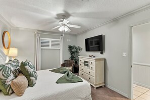 A bedroom with a bed, a dresser, a television, and a ceiling fan.