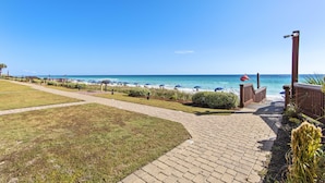 A paved pathway leading to a beach with umbrellas and a clear view of the ocean.