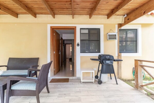 A covered patio area with wicker furniture, a barbecue grill, and a door leading to an interior space.