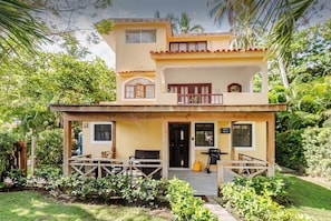 A two-story house with a balcony, a porch with wooden railings, and a small garden area.