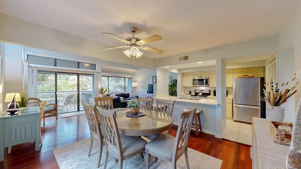 A spacious living room with a large round table, a ceiling fan, and a view to the outside.