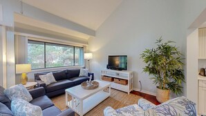 A modern living room with a sofa, coffee table, TV, and a large potted plant. - Perfect Location for a Family Vacation! (Hilton Head)