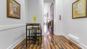 A hallway with wooden flooring, framed artwork on the walls, and a table with chairs.