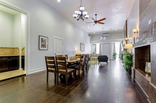 A spacious dining area with a long table and chairs, a chandelier, and a ceiling fan.