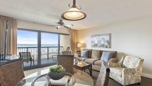 Ein geräumiges Wohnzimmer mit Balkon und Meerblick, ausgestattet mit einer Couch, Sesseln und einem Couchtisch.
