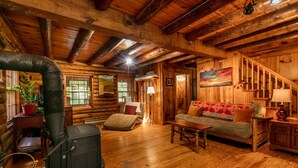 A cozy log cabin interior with a wood-burning stove, a sofa, and a staircase. - Dupont Forest Trailside Cabin (Hendersonville)