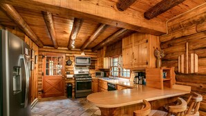 A log cabin kitchen with a refrigerator, stove, microwave, and wooden bar seating. - Dupont Forest Trailside Cabin (Hendersonville)