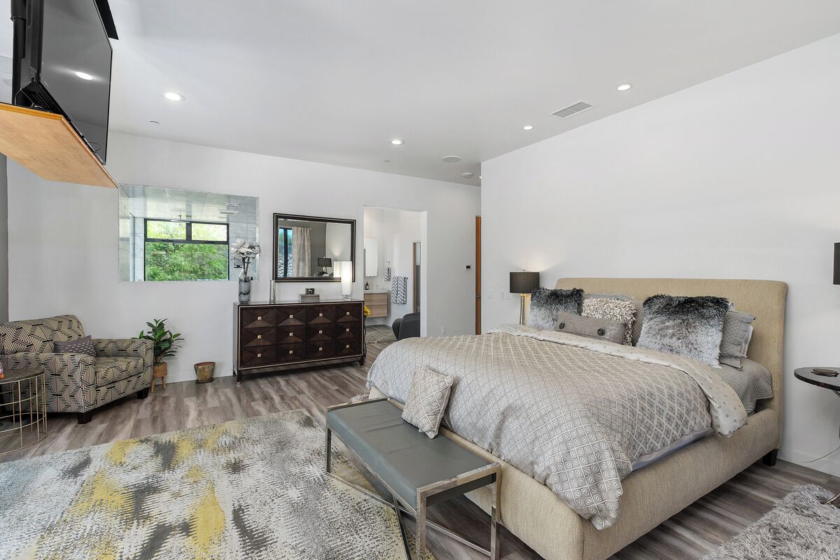 A modern bedroom with a large bed, a sofa, a dresser, and a TV mounted on the wall.