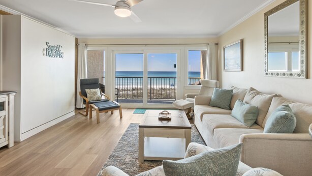 Un salon spacieux doté d’une grande fenêtre donnant sur la plage, d’un ventilateur de plafond et d’un coin salon confortable.