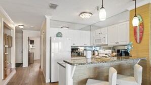 Une cuisine moderne avec des meubles blancs, un plan de travail en granit et un coin bar équipé de deux tabourets de bar blancs.