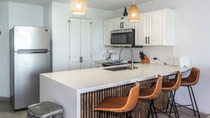 Een moderne keuken met witte kastjes, roestvrijstalen apparatuur en een centraal kookeiland met barstoelen.