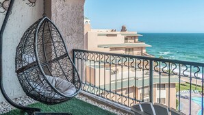 Een balkon met een hangstoel, uitzicht op de oceaan en een gebouw met een groen dak.