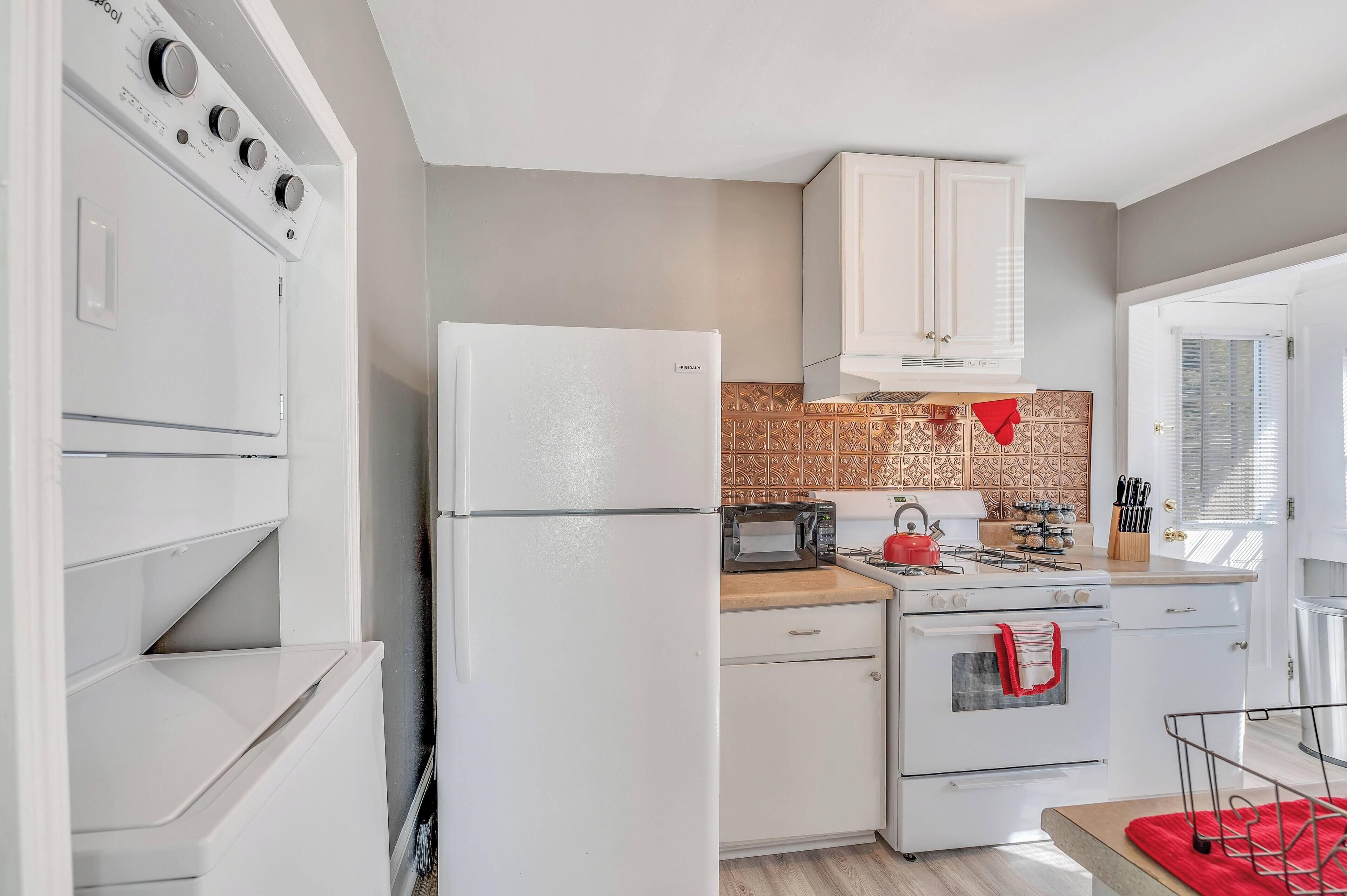 A compact kitchen with white appliances, a patterned backsplash, and a window with blinds.