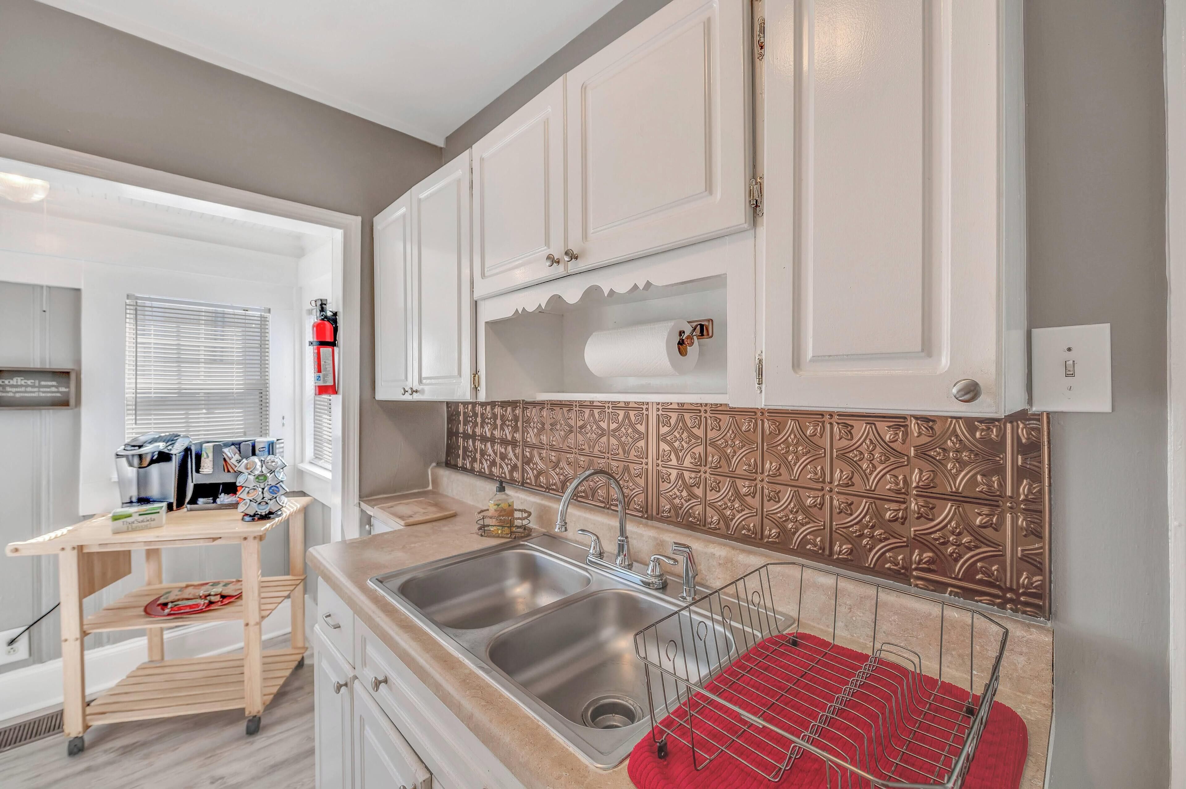 A kitchen with white cabinets, a stainless steel sink, a red towel rack, and a coffee machine.