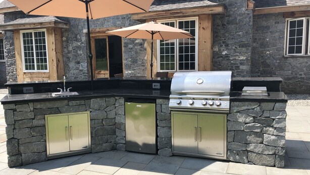 A stone-built outdoor kitchen with a built-in grill, a sink, and a large umbrella providing shade. - Greystone Manor - An isolated 30 Acres in Stowe,  with Hot Tub!!! (Stowe)