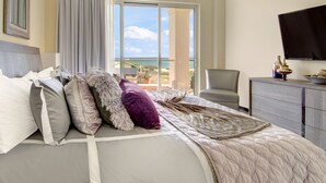 Habitación de hotel con cama, televisión, escritorio y vista al océano a través de una puerta corrediza.
