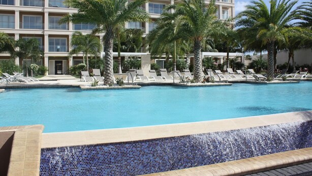 Zona de piscina de hotel con sillones de descanso y palmeras.