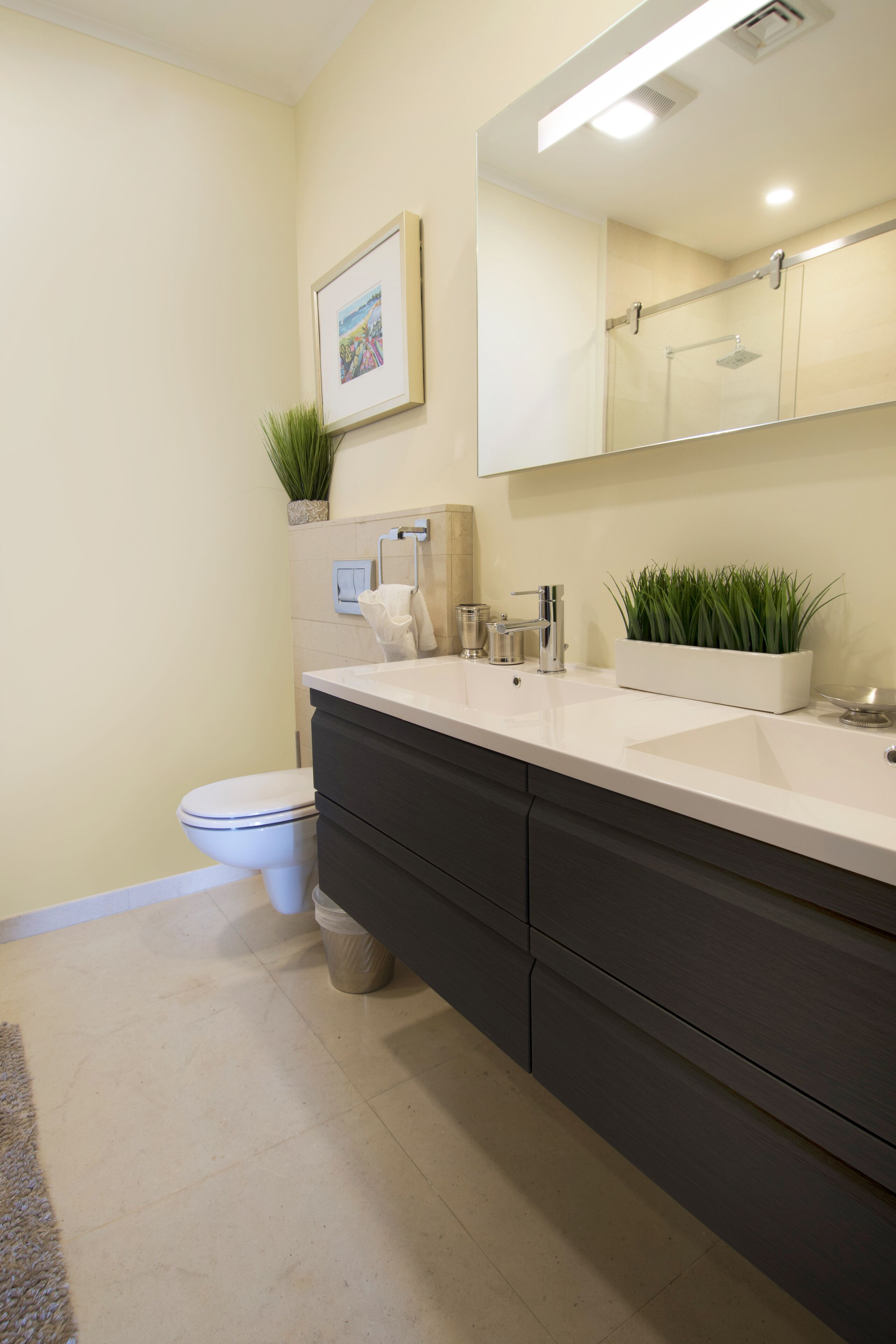 Une salle de bain moderne avec un lavabo blanc, un meuble-lavabo foncé et un grand miroir.
