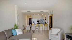 Una sala de estar moderna con un sofá y un sillón, un comedor con sillas amarillas, y una cocina al fondo.