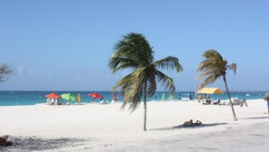 Una playa de arena blanca, palmeras y sombrillas coloridas.