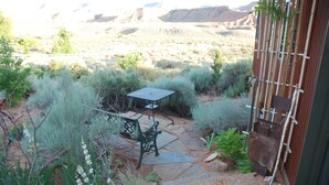 Un patio con mesa y sillas, rodeado de vegetación desértica y vistas a las montañas.