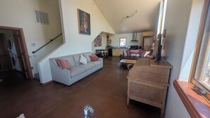 Amplia sala de estar con un sofá gris, una mesa de centro de madera y una cocina al fondo.
