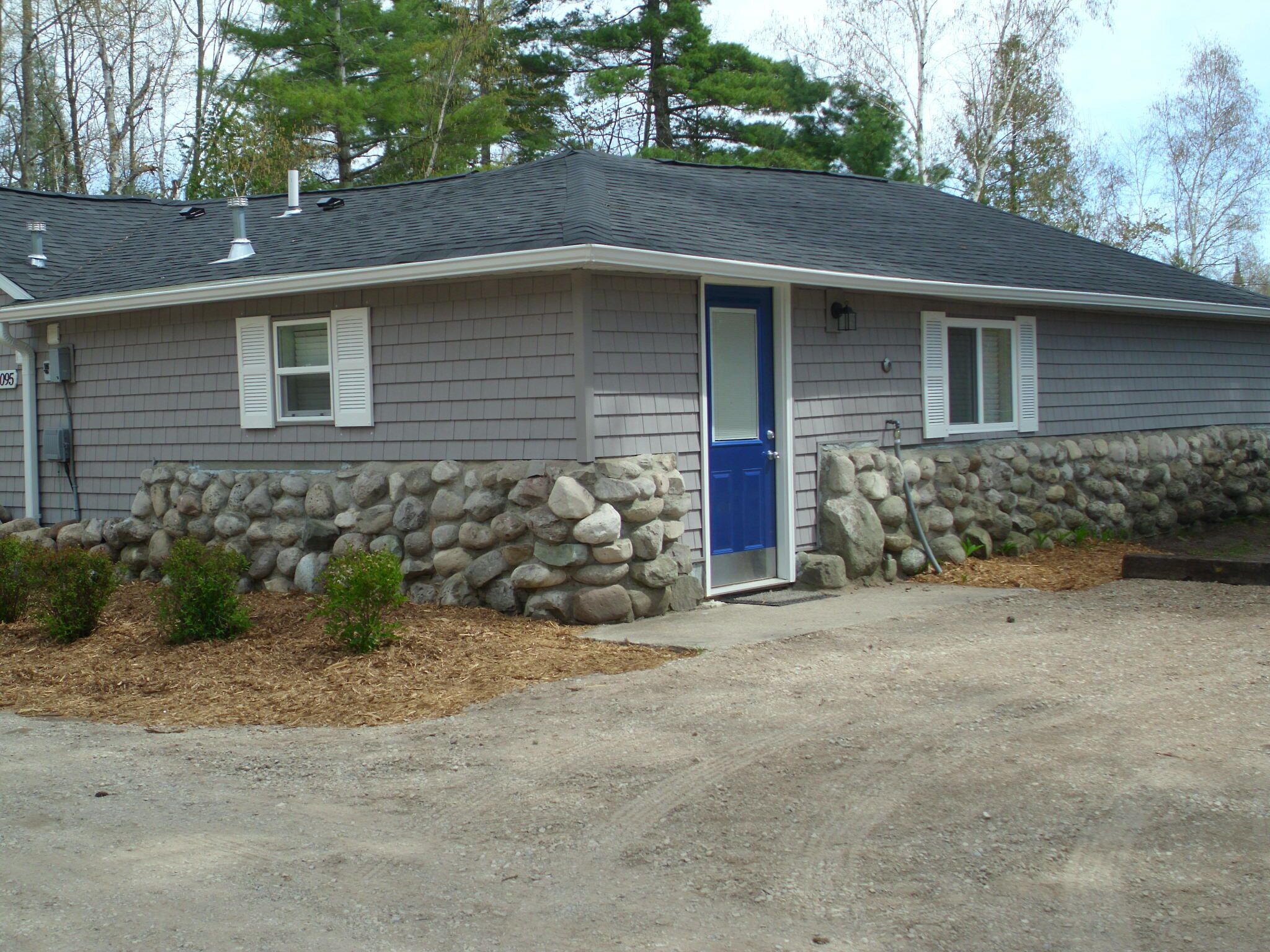 A single-story house with a stone foundation, a blue door, and a gray exterior.