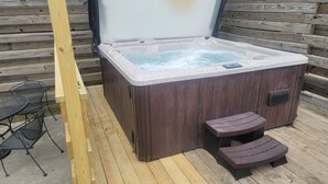 Ett bubbelbad med träpanel på utsidan, två trappsteg som leder upp till det, och ett metallbord och en stol i närheten.