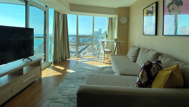Una sala de estar moderna con un televisor grande, un sofá y un comedor con mesa y sillas.