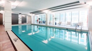 Una piscina interior con agua cristalina, suelo de baldosas y vistas al exterior a través de amplias ventanas.