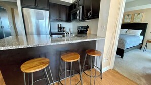 Una cocina moderna con armarios oscuros, electrodomésticos de acero inoxidable, encimera de granito y tres taburetes de madera.