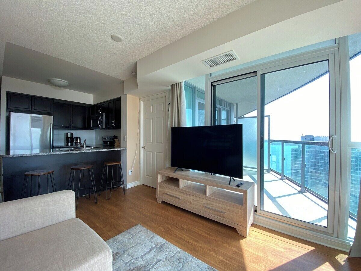 A modern apartment with a kitchen, a living area with a TV, and a balcony with a city view.