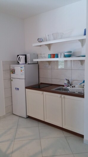 A compact kitchen with white cabinets, a built-in microwave, a sink, and a small shelf with cups and a kettle. - Villa Allegra in Lovran, Comfort Apartment 104, Balcony-Sea view (Lovran)